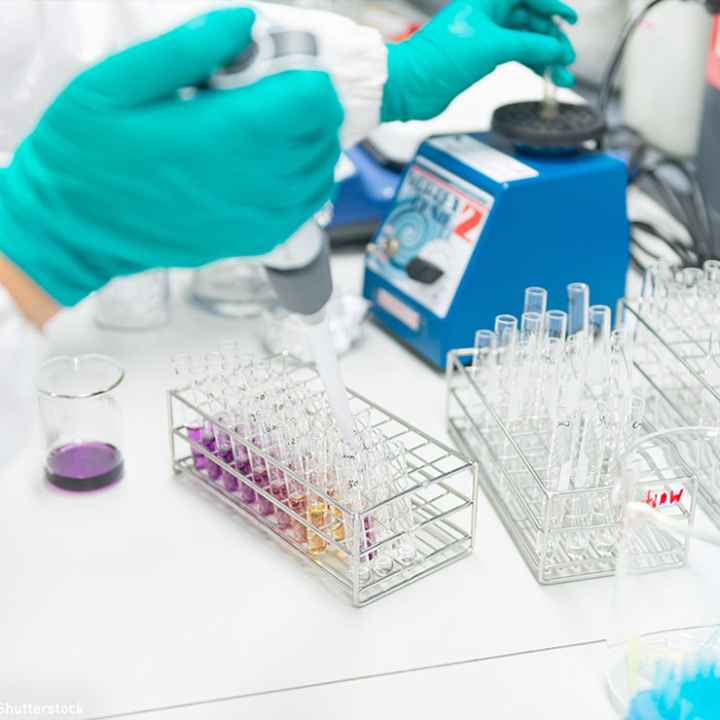 A gloved hand injects fluid into a test tube.